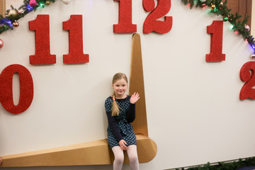 little girl sitting on the hand of a large decorative clock, 11:45 PM, without 15 minutes new year