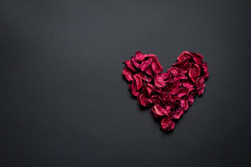 Obraz premium Red petals formed in the shape of a heart on a black background, congratulations concept