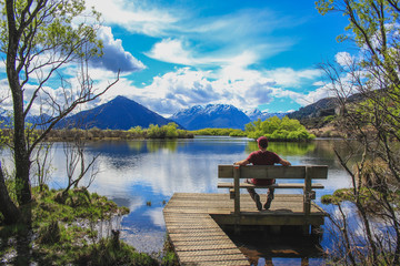 Young man is sitting next to Glenorchy Lagoon in Glenorchy, South Island, New Zealand