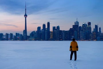 Schilderijen op glas Man walking in fresh snow on frozen Lake Ontario with Toronto city skyline in winter © Reimar