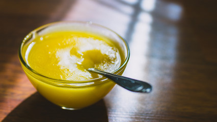 Round glass bowl with sweet honey and spoon on a sunny wooden table.