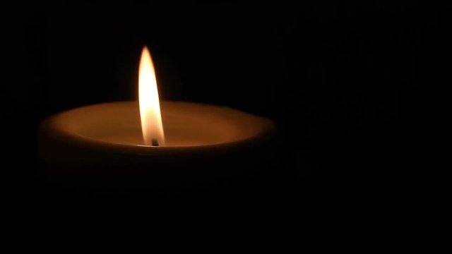 A single pillar candle burning with a flickering flame lights the darkness - great copy space in a seamlessly looping video