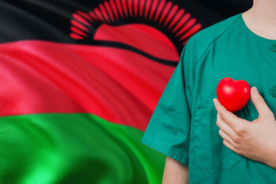 Malawi Veterinary Clinic Concept. Veterinarian Is Holding Plastic Heart In Green Uniform On National Flag Background. Animial Love Theme.