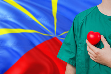Reunion veterinary clinic concept. Veterinarian is holding plastic heart in green uniform on national flag background. Animial love theme.