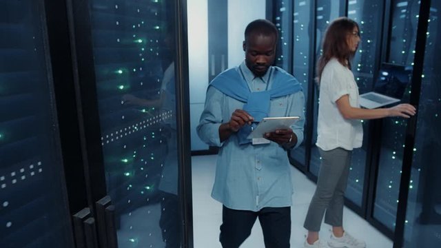 Team of data center doing web hosting connections operation inside server cabinet. Diverse male and female IT workers cooperating in backup diagnostics of database.