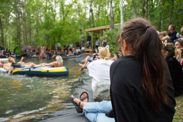 Young Woman Sits by Pond at Music Festival with Crowd in Summer