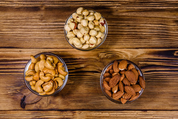 Various nuts (almond, cashew, hazelnut) in glass bowls on a wooden table. Vegetarian meal. Healthy eating concept. Top view