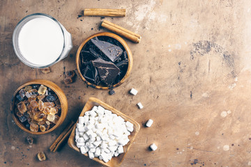 Ingredient for hot chocolate with pieces of chocolat, cinnamon, brown sugar and marshmallows on a rustic background. Top view. Flat lay