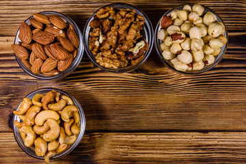 Various nuts (almond, cashew, hazelnut, walnut) in glass bowls on a wooden table. Vegetarian meal. Healthy eating concept. Top view