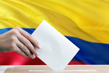 Colombia election concept. Side view woman putting a ballot in a box on national flag background.