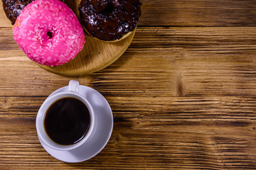 Cutting board with glazed donuts and cup of coffee on a wooden table. Top view