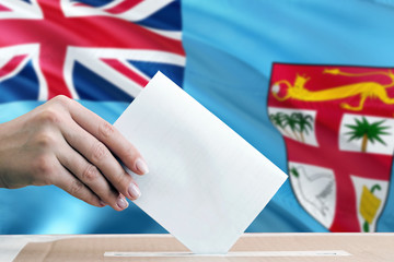 Fiji election concept. Side view woman putting a ballot in a box on national flag background.