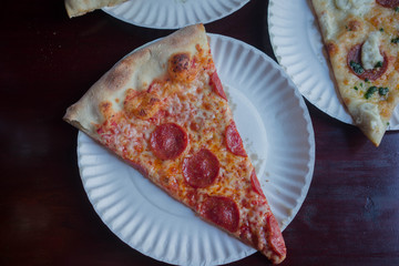 close up of a pepperoni pizza on a white plate with pizza in the background