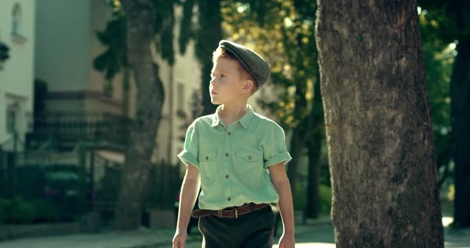 Nice Caucasian little boy in hat and retro style walking the street and looking around on a nice sunny summer day. Outdoor.