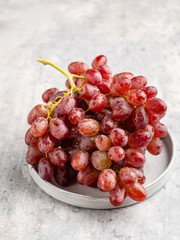 A bunch (cluster) of ripe red (purple) grapes with the drops of water on it on gray ceramic plate on light gray background. Top view. Layout template. 