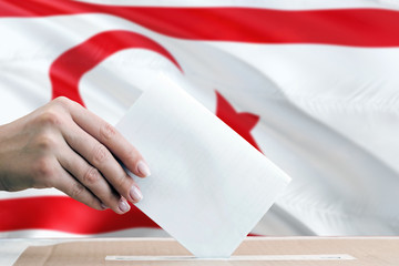 Northern Cyprus election concept. Side view woman putting a ballot in a box on national flag background.