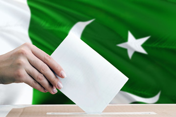 Pakistan election concept. Side view woman putting a ballot in a box on national flag background.