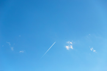 Small clouds and airplane white track or plane line on a blue sky background, copy space