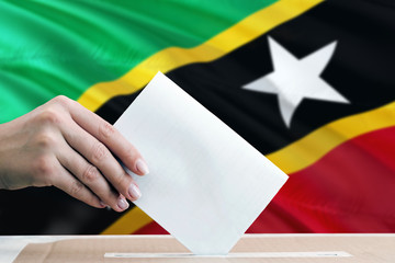 Saint Kitts And Nevis election concept. Side view woman putting a ballot in a box on national flag background.