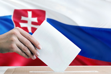 Slovakia election concept. Side view woman putting a ballot in a box on national flag background.