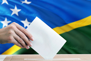 Solomon Islands election concept. Side view woman putting a ballot in a box on national flag...