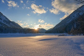 beautiful sunset in the mountains Alps in winter - with a blue yellow heaven - sunset between the mountains  Germany Lödensee - sun star - reflection in snow - winter landscape