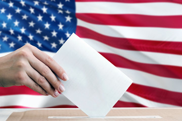 United States election concept. Side view woman putting a ballot in a box on national flag background.