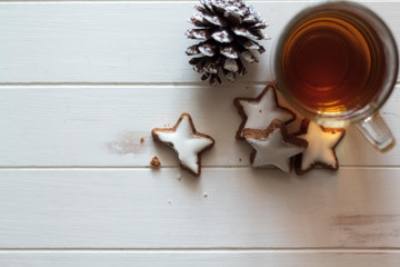Top view of cup of tea with star-shaped cookies and a pine cone on a white wooden table. With copy space