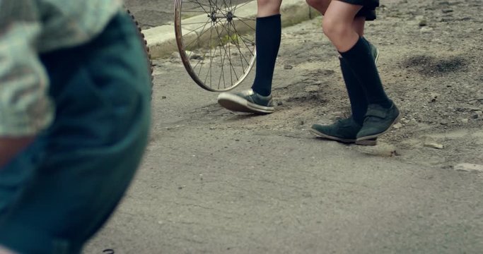 Close up of the tire and wheel rolling on the street road while small Caucasian hooligans boys playing with them. Outdoors.