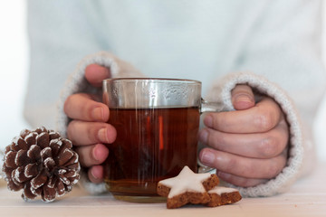 Woman holding tea with star shaped cookies and pine cone on wooden table
