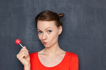 Obraz premium Portrait of thoughtful blond girl holding pink lollipop in one hand
