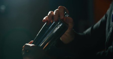 Close up of a professional bartender is preparing an alcoholic cocktail with ice cubes in a shaker to customers at the bar or disco club.