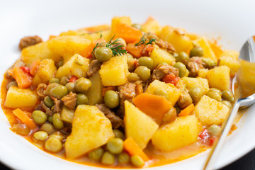 pea dish with potatoes, carrots and meat in white plate