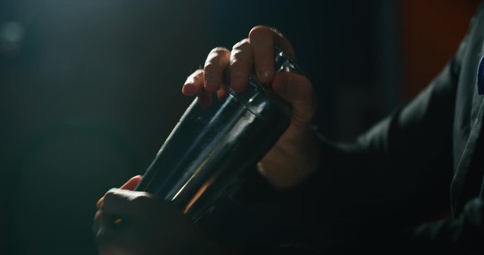 Close up of a professional bartender is preparing an alcoholic cocktail with ice cubes in a shaker to customers at the bar or disco club.