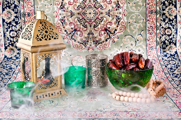Ramadan lamp, candles, dates in green bowl and rosary with smoke.