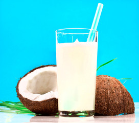 Coconut with leaves and milk in a glass isolated on a cyan background.