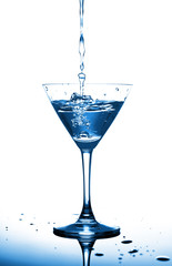 Trendy blue monochrome image with transparent alcoholic coctail in classic coctail glass with a splash on white. Merry Christmas and a Happy New Year 2020!