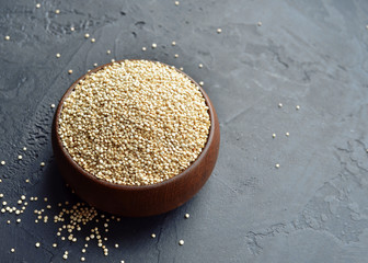 Organic dry quinoa grains in wooden bowl on black stone background, copy space, top view