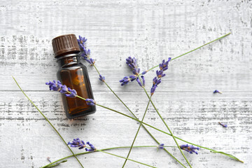 Organic lavender oil in dark glass bottle and fresh lavender flowers on old wooden background....