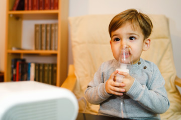 Little small sick boy using steam inhaler nebulizer mask inhalation at home. Medical procedures...