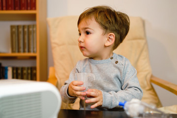 Little small sick boy using steam inhaler nebulizer mask inhalation at home. Medical procedures...