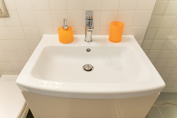 Modern bathroom sink / tap - orange soap container and glass. Metal tap.