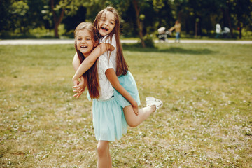 Fototapeta premium two cute little girls in white T-shirts and blue skirts play in the summer park
