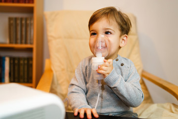 Little small sick boy using steam inhaler nebulizer mask inhalation at home. Medical procedures...