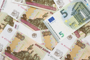 A close up image of a five Euro bank note from Europe in macro with a bed of Russian one hundred ruble bank notes
