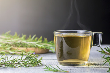 Glass cup of healthy rosemary tea with fresh rosemary bunch on white wooden rustic background,...