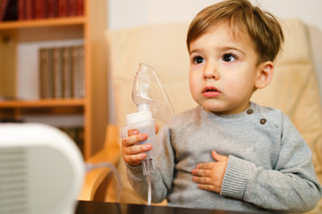 Little small sick boy using steam inhaler nebulizer mask inhalation at home. Medical procedures...