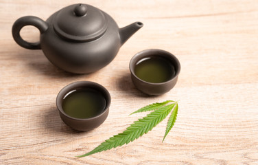 Tea made from cannabis leaves ,A glass of hot marijuana tea on wooden table , tea pot and cups on wooden table ,