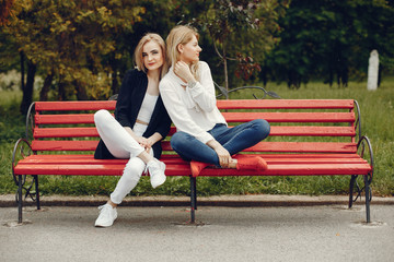 Pretty girls in a summer park. Friends sitting on a bench. Ladies with blonde hair