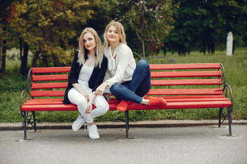 Pretty girls in a summer park. Friends sitting on a bench. Ladies with blonde hair